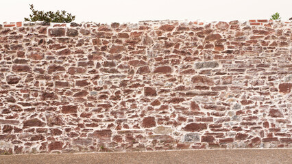 Muro de piedra rocosa rojiza en centro de pueblo europeo