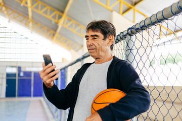 Physical activity in old age. 70 years old man using smartphone while exercising