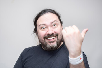 An unshaven man with bracelets in the colors of the Japanese flag gestures with his thumb to the side. Selective focus on the bracelet.
