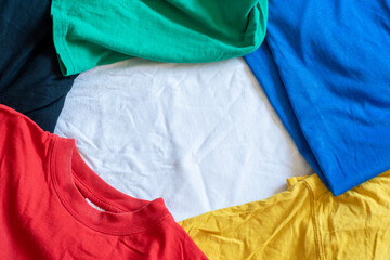 Background and casually lying multi-colored t-shirts with empty space for text in the middle. Template with cotton fabric.