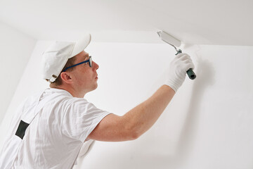 Painter worker with roller painting ceiling surface into white