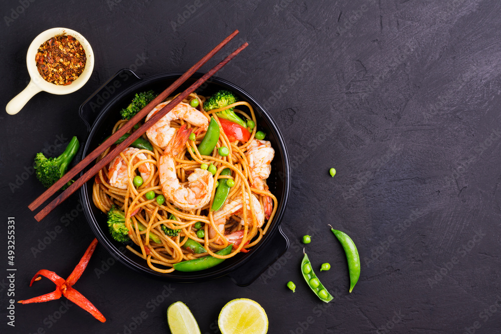 Sticker stir-fried spaghetti or stir-fry noodles with vegetables and shrimp in a black bowl. dark background