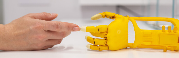 Woman's hand and a plastic hand prosthesis for a child on a white background. 