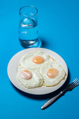 Fried eggs on a blue background. Three fried eggs on a plate. Quick and tasty breakfast