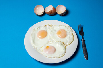 Fried eggs on a blue background. Three fried eggs on a plate. Quick and tasty breakfast