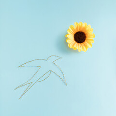Swallow made of branches flying toward sunflower on pastel blue background. Minimal spring composition. Nature flat lay aesthetic.