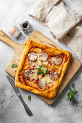 Homemade puff pastry pizza with salami, mozzarella, tomatoes and basil on the kitchen table....