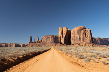 A dirt road straight into distant classic southwest desert landscape in Monument Valley in Utah and...