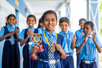 Proud girl with winner trophy and medal with cheeful students applauding for success of kid -...