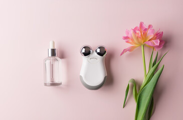beauty serum and microcurrent toning device on color background with flower. beauty cosmetic product for skin care. top view