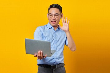 Portrait of cheerful young asian man Asian in glasses using a laptop, doing a video call, gesturing...