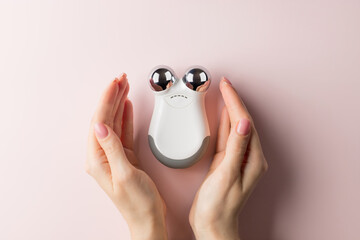 microcurrent facial toning device with female hands on color background. Beauty, skincare, cosmetology concept. top view