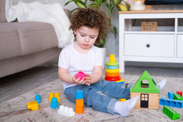 Naklejka premium curly child girl playing with pyramid and constructor at home. early children development