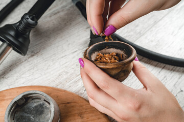 Filling a hookah bowl with tobacco on a gray background