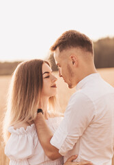 Handsome guy and blonde girl walking on the field of wheat on a beautiful warm sunset.