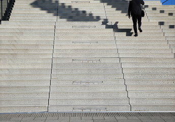 View on empty monotone concrete steps with one single man in black business suit walking upwards -...