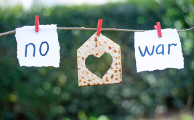 Notes with words "No", "war" and Matzah in shape house with heart on blurry green background. World without war, Love and world on planet. Peaceful sky