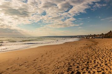 Santa Marinella, Rome, Lazio, Italy - Sea shore of the Roman coast of Santa Severa on a winter day. Many people stroll and enjoy the sun on the beach, at sunset. Rough sea, wind, cloudy blue sky