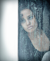 When its more than just the blues. A sad young woman sitting by a window while its raining outside.