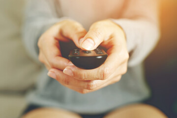 close up Television remote control in casual man hand hold pointing to tv set and turning it on or...