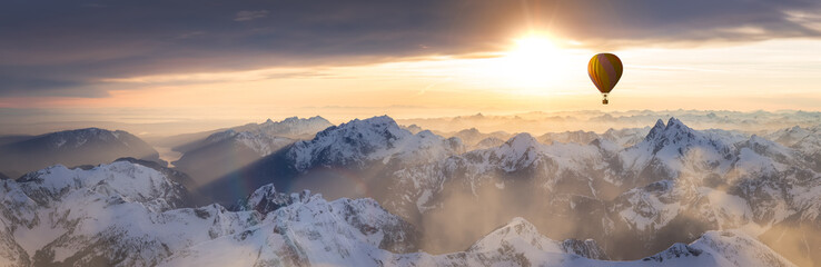 Dramatic Mountain Landscape covered in clouds and Hot Air Balloon Flying. Adventure Composite Dream Concept Artwork. Aerial Image from British Columbia, Canada. Colorful Sunset Sky