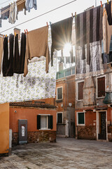 Laundry hanging out of typical Venetian facade,Italy.Narrow street with colorful buildings and clothes dry on rope,Venice.Clean clothes drying outdoors in small square.City lifestyle,urban scene.