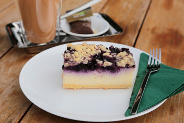 weißer Teller auf einem Holztisch mit Streuselkuchen, Blaubeerkäsekuchen mit streusel