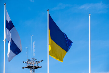 Ukrainian and Finnish flags waving in the wind against a bright blue background. A tall radio...