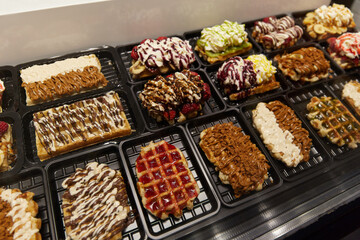 Various of traditional Belgian waffles topped with chocolate, speculoos, whipped cream and fruit display in a storefront in Brussels