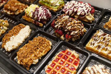 Various of traditional Belgian waffles topped with chocolate, speculoos, whipped cream and fruit display in a storefront in Brussels