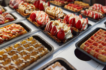 Various of traditional Belgian waffles topped with chocolate, speculoos, whipped cream and fruit display in a storefront in Brussels