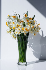 Fototapeta na wymiar A bouquet of white daffodils in glass vase on the table, natural sunlight. Narcissus flowers in minimal close up composition with visible petal texture. Background, copy space top view.