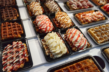 Various of traditional Belgian waffles topped with chocolate, speculoos, whipped cream and fruit display in a storefront in Brussels