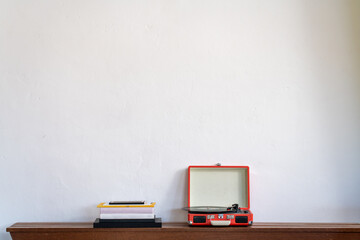 Pile of books and a retro turntable on a wooden shelf against a white wall. Record player. High...