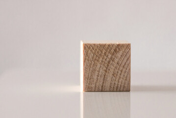 Single wooden cube on reflective surface. White background.