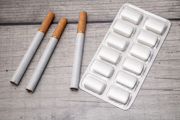 A blister pack with nicotine gum and three cigarettes on a wooden background as a symbol of smoking cessation