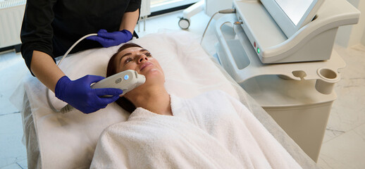Beautiful middle aged woman receiving an anti-aging treatment on her face with modern laser...