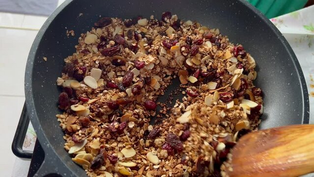 Stirring granola with dry berries in a frying pan. Cooking home made granola from oats and honey. Healthy breakfast with cranbeeries and raisin.
