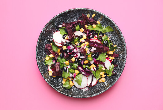 Bowl of Mexican vegetable salad with black beans and radish on pink background