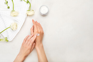 Woman applying cream onto hand on light background