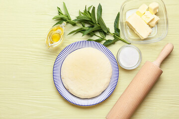 Plate with dough for preparing lazy dumplings, ingredients and rolling pin on color wooden background