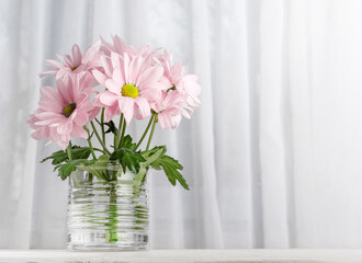 A flowering branch of chrysanthemums in a glass against the background of a window. Copy space