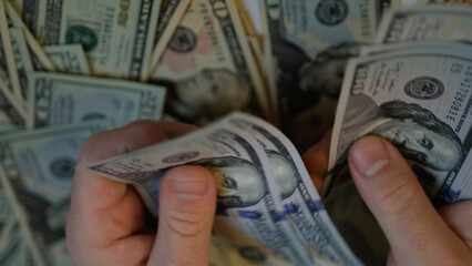 Men's hands count 1000 American one hundred dollar bills against the background of smaller bills of...