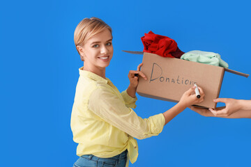 Young woman with box writing word DONATIONS on blue background