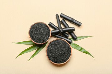 Bowls of activated carbon powder, black bamboo sticks and leaves on color background