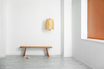 Wooden bench, slippers and hanging lamp near light wall