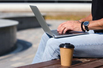 Young man using laptop on bench outdoors, closeup