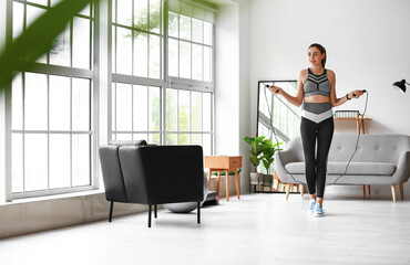 Sporty young woman jumping rope at home