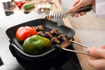 Female chef with tongs frying tasty vegetables in kitchen, closeup