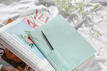 Stylish notebook with newspaper, magazine and gypsophila flowers on white fabric background